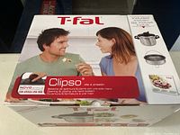 Box front showing T-fal Clipso pressure cooker branding with couple and product images.