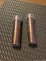 Two clear plastic tubes each filled with a roll of coins, standing upright on a textured surface.
