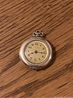 Top-down photo of the Waltham rolled gold plated pendant watch on a wooden surface, showing dial, numerals, and watch crown