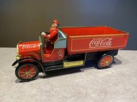 Side front view of the Coca Cola tin truck showing the driver figure, detailed wheels, and Coca Cola branding on the truck bed and front.