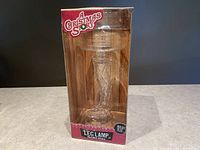 Clear molded glass drinking glass shaped like leg lamp from A Christmas Story shown with original retail box.