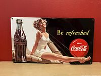 Front image of the metal sign showing the woman in a white swimsuit, Coca-Cola bottle, and text 'Be refreshed'.
