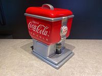 Front-side view of the Coke dispenser cookie jar showing red and silver ceramic design with 'Drink Coca-Cola Ice Cold' and 'Have a Coke' on dispenser handle.