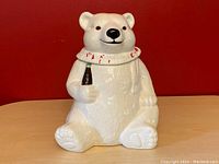 Front view of white ceramic polar bear cookie jar holding a coke bottle, with collar lid