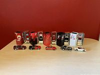 Photo of all six Johnny Lightning diecast cars lined up in front of their Coca Cola branded tin boxes, showing various angles.