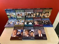 Front view of all 14 DVD box sets of Dallas TV show, arranged in two rows showing cover art.