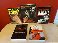 Front view of all five martial arts/karate books arranged on a table against a red wall.