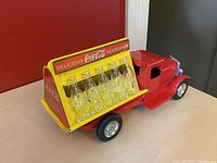 Side angle of red Metalcraft by Gearbox Coca-Cola truck with twelve glass Coca-Cola bottles arranged in yellow branded display area.