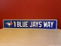 Front view of the MLB Toronto Blue Jays licensed street sign against a red background, showing the full text and logo.