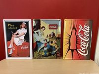 Front view of the three Coca Cola tin picture signs with vintage advertising images.