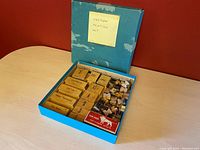 Photo of open blue box containing various yellow wooden boxes of cartoon stamps, small ruler, and ink pad with a label 'Cartoon Printing Set' on box lid.