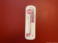 Front view of vintage Coca-Cola white enamel thermometer showing full temperature scale and graphics.