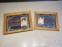 Two wooden framed vintage Coca Cola mirrors side by side on a countertop showing the full design and wood frame.