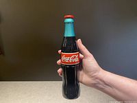 Front view of the metal door handle shaped like a vintage Coca Cola glass bottle, showing label and colors in hand for scale.