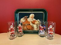 Front view of the Coca Cola tray and all four glasses arranged in front on a table with red background