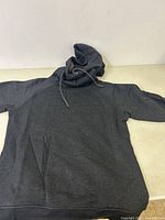 Full view of a dark gray hoodie laid flat showing hood with drawstrings and front pocket.