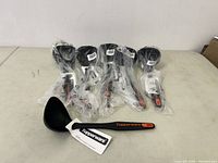 Six new Tupperware laddles in sealed plastic packaging, lined up together.