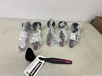 Six Tupperware ladles in individual plastic packaging, black with pink branding on handles, laid out on a white surface.