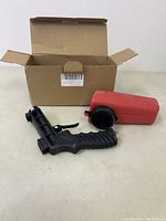 Sandblast kit parts on a light surface including black pistol grip handle and red container tank with open box behind
