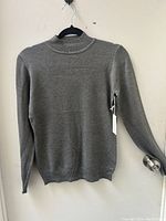Front view of soft gray knitted sweater with long sleeves and mock neck, hanging on a black hanger.