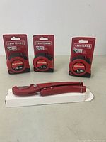 Three red Craftsman measuring tapes in packaging and one red PEX pipe cutter tool, all new.