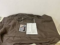 Overview of the brown fabric patio cover laid flat, displaying included pamphlets and instruction sheet.