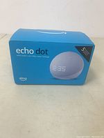Front view of sealed Echo Dot box showing clock display illustration, branding, and Alexa logo.