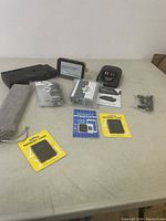 Overview of lot with memory cards in yellow packaging, black multi-port charging dock, several small electronic accessories, plastic cases, cables, and assorted hardware parts on a table.