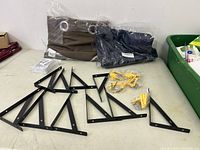 Black metal shelf brackets with yellow wall plugs and screws on a table next to packaged curtains.