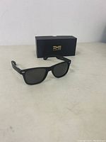 Overall view of Luenx black sunglasses positioned next to the branded box on a flat surface