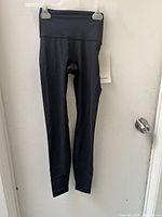 Black Lululemon yoga pants hung on hanger against door.