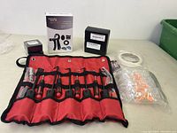 Photo of the lot showing the adjustable counting grip kit box, a red hook set pouch with multiple hooks and tools, a black box, white tape, and a clear package of orange earplugs.