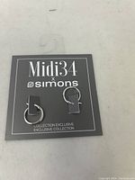 Photo showing the pair of Simons Midi34 sterling silver hoop earrings on black display card labeled Midi34 x Simons Exclusive Collection.