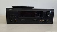 Front view of Denon AVR-391 receiver showing control buttons, large display window, and volume knob with remote placed on top.