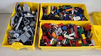 Top view of three yellow plastic containers filled with a mix of gray, black, red, green, and multicolored LEGO bricks and parts