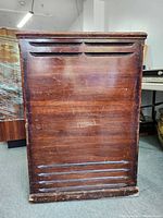 Front view of dark brown wooden cabinet with horizontal vent slats and surface wear