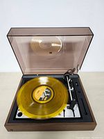 Open dust cover showing yellow transparent vinyl record on turntable platter with control panel and tonearm visible.