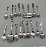 Overview of 17 souvenir spoons laid in two rows on flat surface