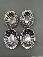 Four oval polished sterling silver nut dishes with ruffled edges laid out on a flat surface.