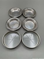 Six silver-rimmed coasters with crystal bases and silver coasters showing decorative rims and polished surfaces.