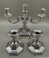 Two antique English silver plate candlesticks with hexagonal bases and one three-arm silver plate candelabra with a square stepped base, displayed against a neutral background.