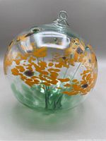 Front angle of the glass ball showing the orange blossom floral pattern and integrated hanging loop at the top.