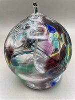 Front view of spherical art glass oil lamp showing colorful internal swirls and clear glass body with wick holder on top.