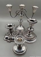 Three single candlesticks and one three-arm candelabra grouped together, showing different designs and finishes.