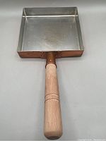 Square copper omelette pan with wooden handle shown from top and side angles, highlighting the pan's shape, material, and condition.