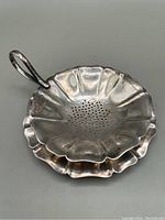 Close-up of the tea strainer bowl showing flower petal shape, holes for straining, and metal handle