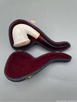 Vintage meerschaum pipe with curved brown stem and white bowl, fitted inside shaped black hard case with red velvet lining and decorative clasp, pipe bowl repaired with usage wear.