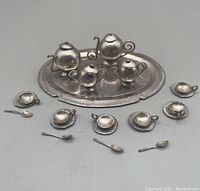 Overview of entire miniature silver tea set arranged on plain surface