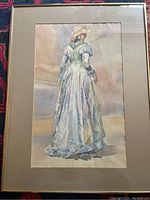 Full view of the framed watercolour painting showing a woman in a detailed blue and cream historical dress with bonnet.