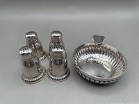 Four Regency style silver plate salt and pepper shakers grouped with a vintage silver plate tastevin bowl with scalloped edges and thumb rest.